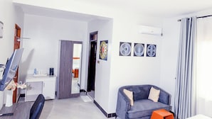 A modern living room with a grey sofa, a flat-screen TV, and a dining area with a table and chairs. - Amani Residence Entebbe (Entebbe)