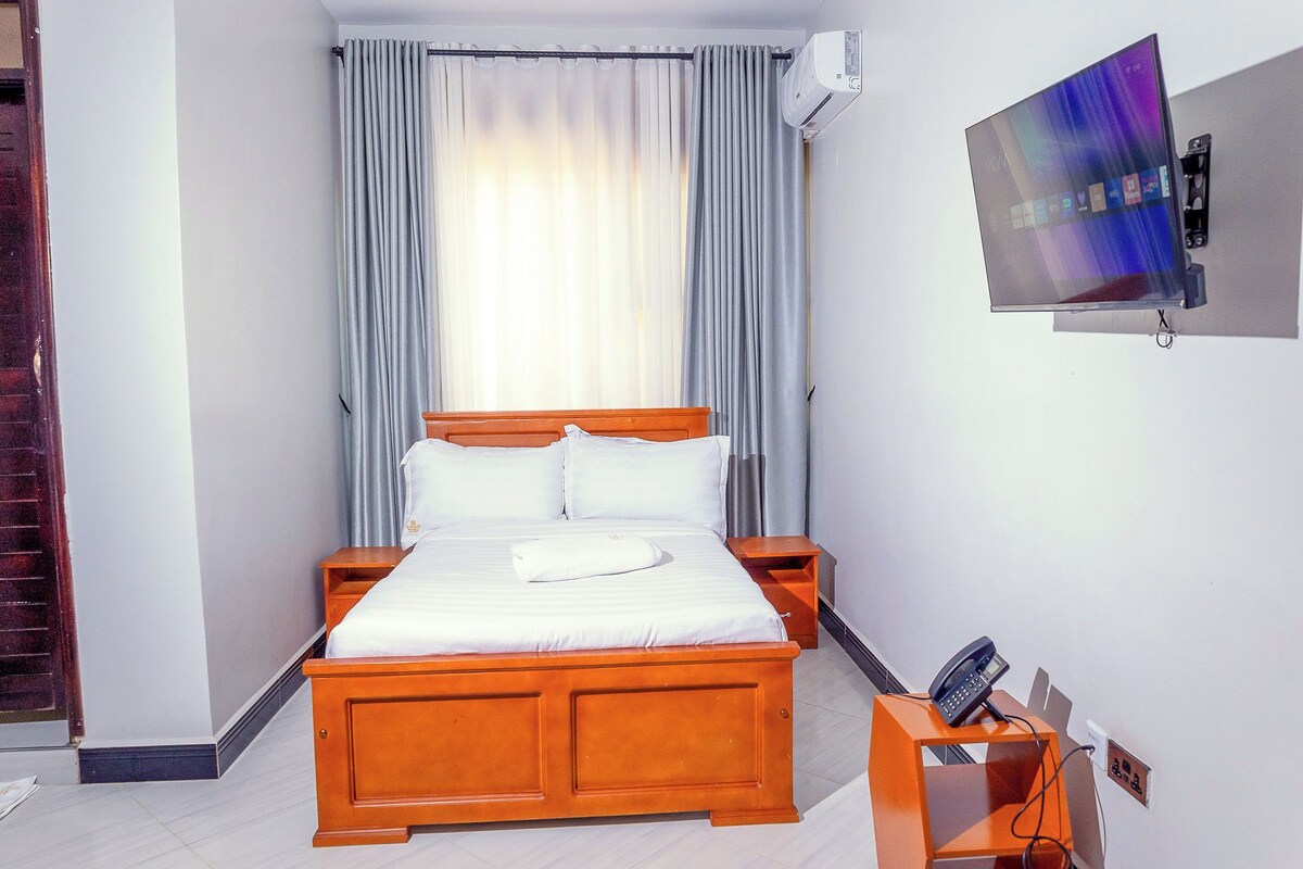 Ein Hotelzimmer mit einem hölzernen Bett, einem an der Wand befestigten Fernseher und einem Telefon auf einem Nachttisch.