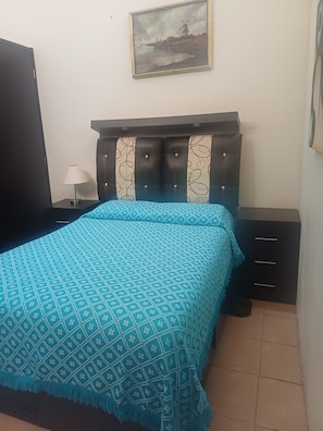 Un dormitorio con cama, mesita de noche, lámpara, armario y un cuadro en la pared.