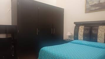 A bedroom with a bed, a wardrobe, a desk, and a lamp.