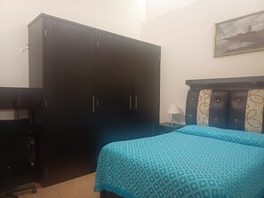 Un dormitorio con cama, armario, escritorio y lámpara.