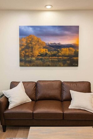 A brown leather sofa with two pillows against a wall, with a landscape painting above it. - West Campus Peaceful Paradise (Fort Collins)