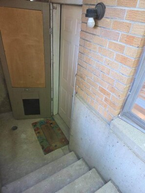 A staircase leading to a door with a doormat, a brick wall, and a light fixture. - West Campus Peaceful Paradise (Fort Collins)