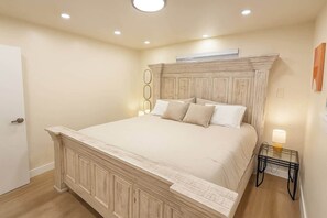 A bedroom with a large bed, a wooden headboard, a bedside table with a lamp, and a door. - West Campus Peaceful Paradise (Fort Collins)