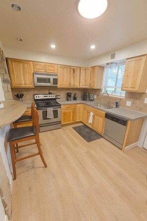 A compact kitchen with wooden cabinets, a stove, a dishwasher, and a sink. - West Campus Peaceful Paradise (Fort Collins)