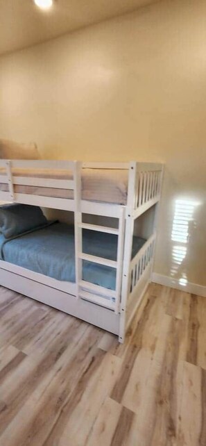 A bunk bed with a mattress and pillows, wooden flooring, and a plain wall. - The Pool house retreat (Osprey)