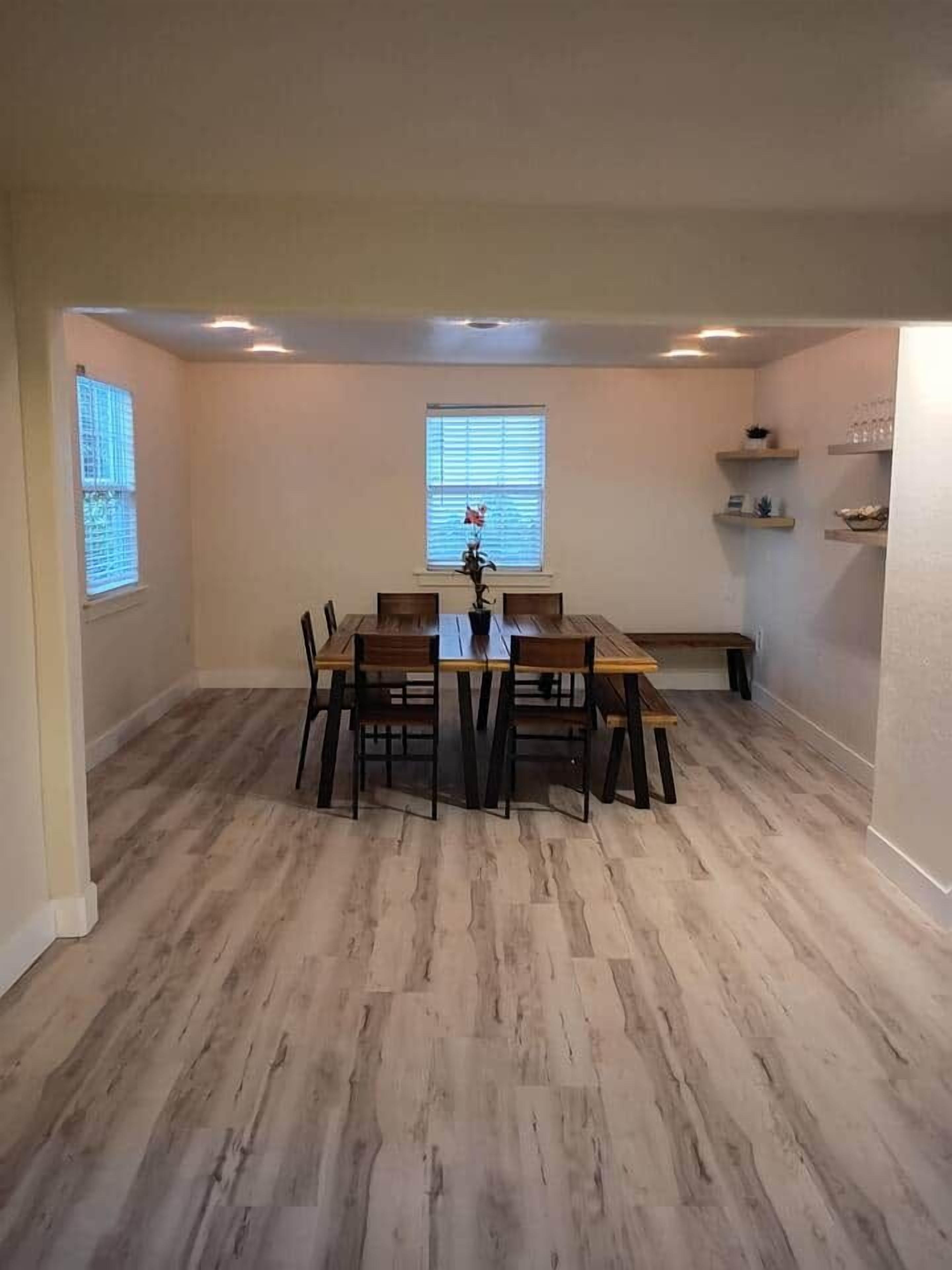 Een eethoek met een houten tafel en stoelen, een bank en een raam met jaloezieën.