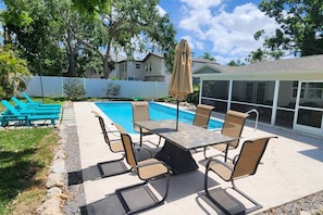 An outdoor pool area with a table and chairs, surrounded by a white fence and trees. - The Pool house retreat (Osprey)