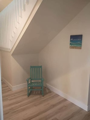 A room with a wooden floor, a green chair, a white wall, and a painting. - The Pool house retreat (Osprey)