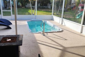 Ein Schwimmbecken mit Whirlpool, umgeben von einer überdachten Terrasse mit Blick auf eine Rasenfläche.