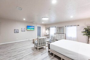 Quarto com cama, duas cadeiras, cômoda, televisão e obra de arte na parede.