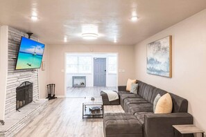 Een woonkamer met een open haard, een ruime bank, een salontafel en een aan de muur bevestigde televisie.