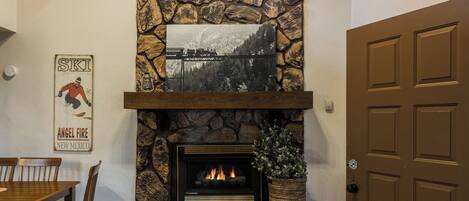 A stone fireplace with a framed picture above it, a dining table with chairs, and a brown door.