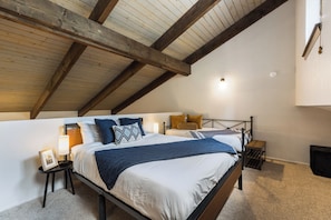 A bedroom with a sloped ceiling, a bed with a headboard, bedside tables, and a nightstand. - Pine Top Loft - Walk to Lifts, Ski Locker, Deck (Angel Fire)