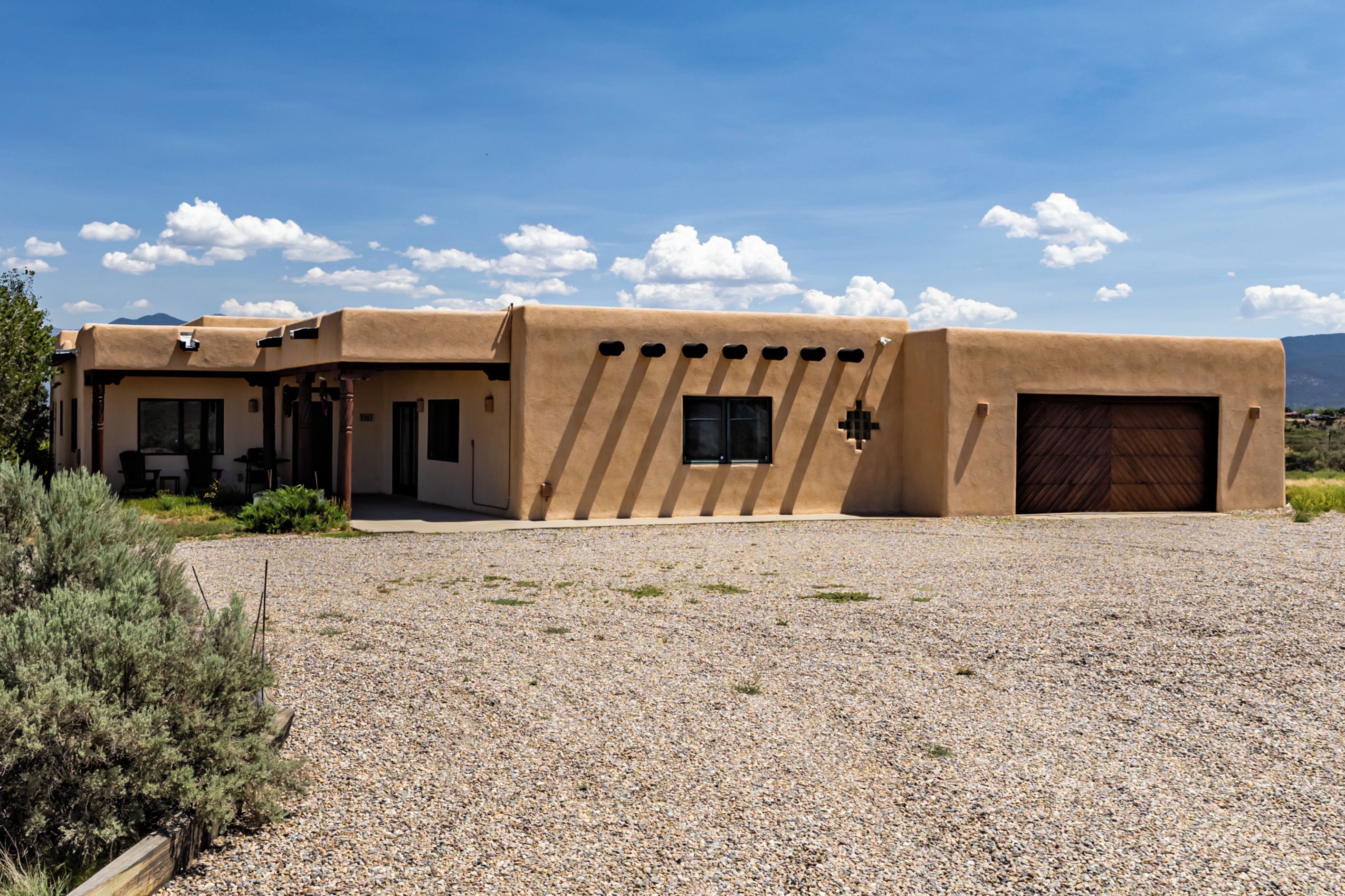 Un bâtiment moderne de style adobe, avec une allée en gravier, un garage et une vue sur les montagnes en arrière-plan.