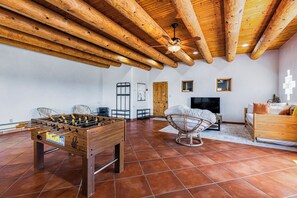 Quarto com teto de madeira, mesa de futebol, televisão e sofá.