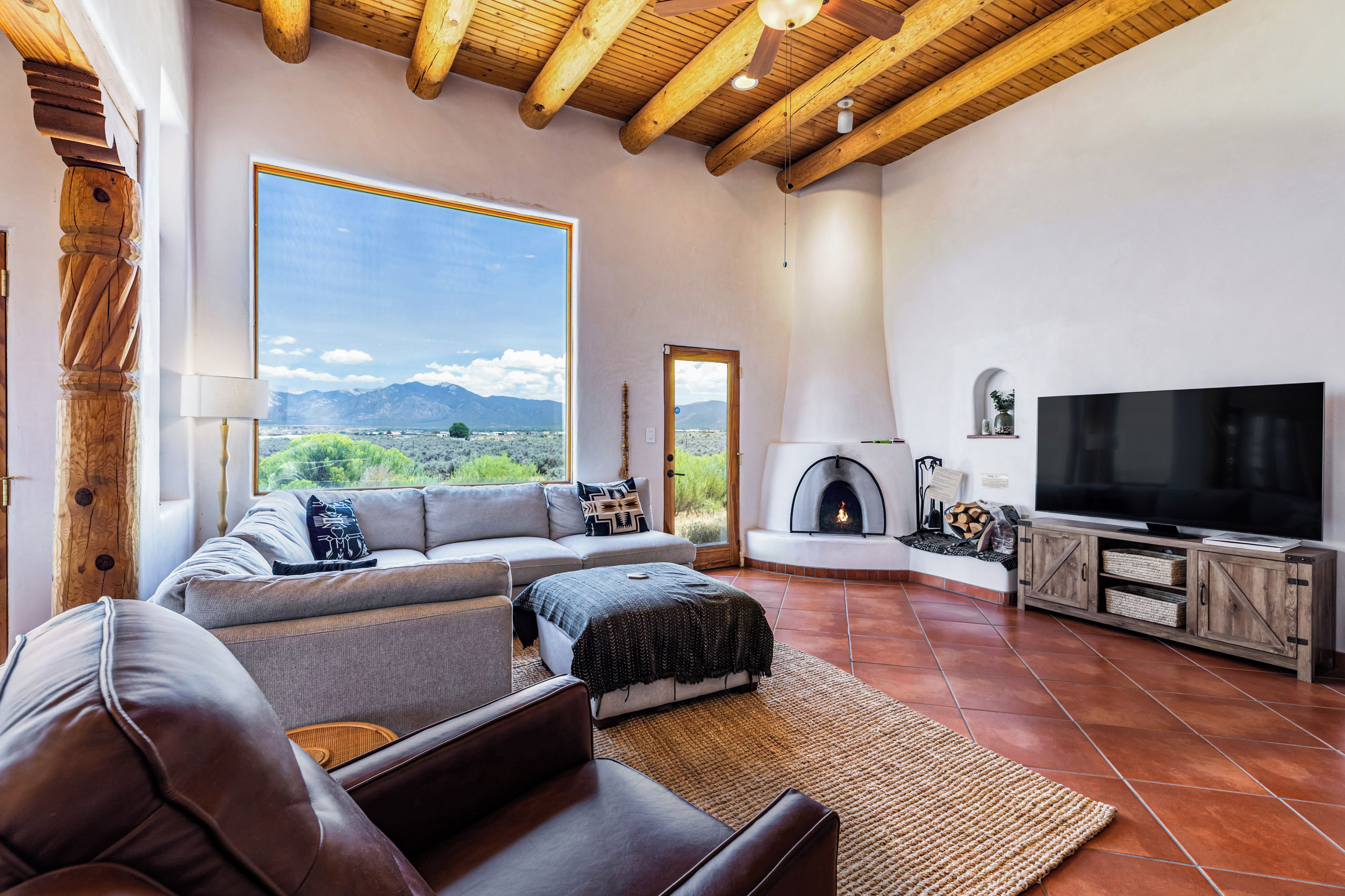 A modern living room with a large window, a fireplace, a television, and a sofa.