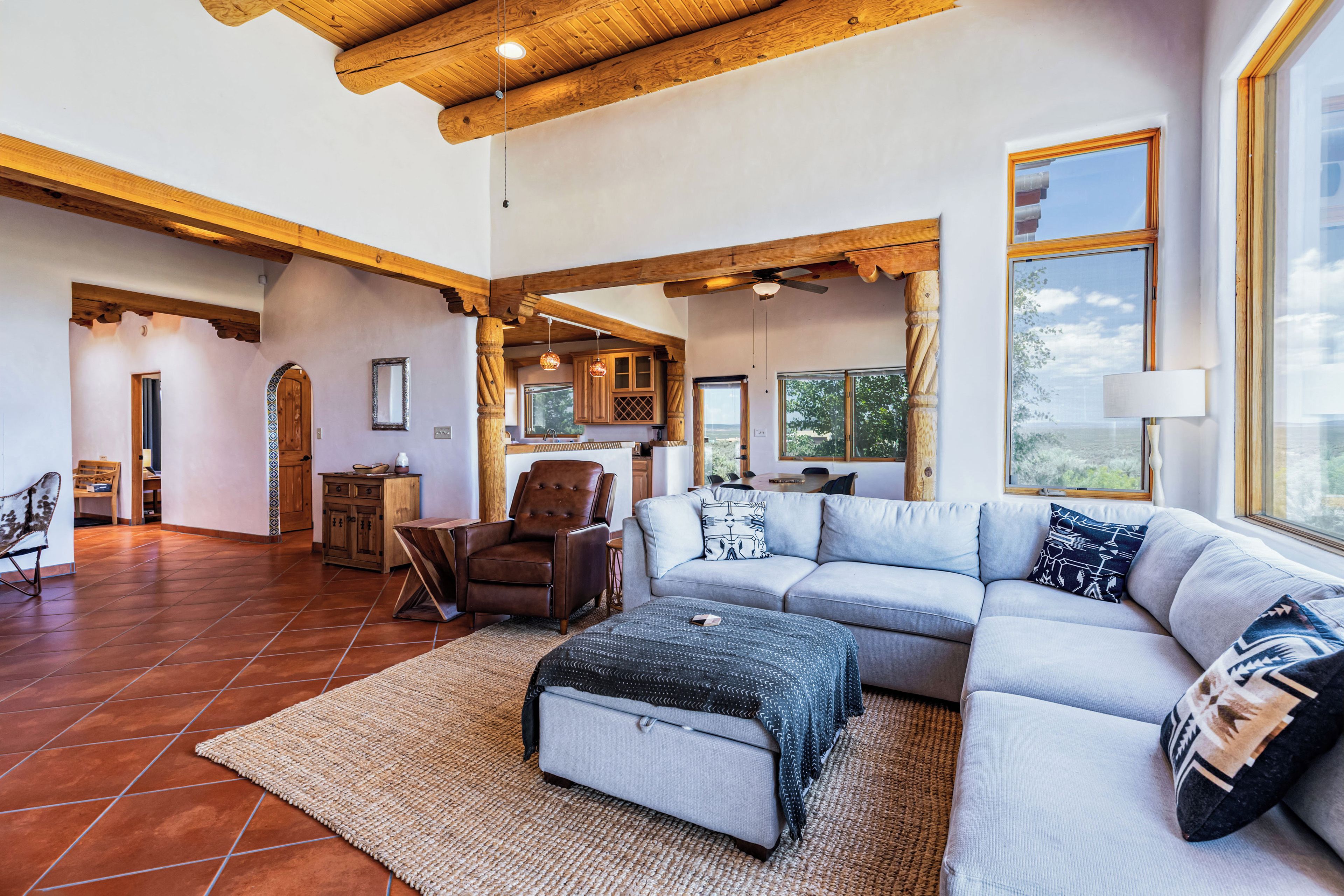A spacious living room with a large sofa, a coffee table, and a fireplace. There is a dining area with a table and chairs visible in the background.