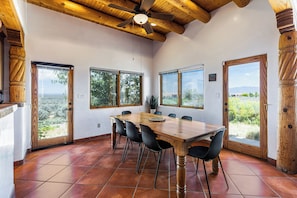 Un comedor con mesa y sillas de madera, ventanas amplias y ventilador de techo.