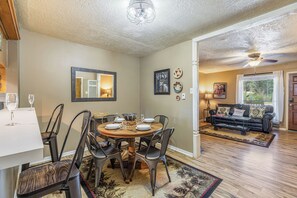A dining area with a round table, chairs, and a view into a living room with a couch and a window. - Tenderfoot Retreat - Creekside, Near Ski & Town (Red River)