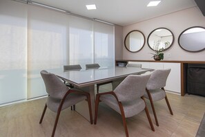 Un salón de conferencias con una mesa de vidrio, cuatro sillas grises tapizadas, una pizarra y una chimenea con una planta en maceta.