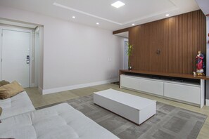 Una sala moderna con un sofá, una mesa de centro blanca, un mueble de entretenimiento de madera y una puerta.
