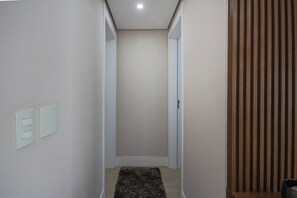 A narrow hallway with a carpeted floor, a door on the right, and a light switch on the left. - 36th floor, Panoramic View - Itaim - 2 suites, 2 parking spaces (São Paulo)