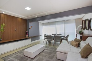 A modern living room with a sofa, a coffee table, a dining area with a table and chairs, and a decorative wall with a plant and a figurine. - 36th floor, Panoramic View - Itaim - 2 suites, 2 parking spaces (São Paulo)