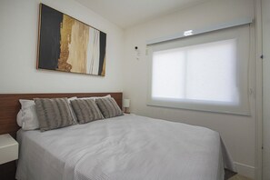 A hotel room with a bed, a nightstand, a lamp, a window with blinds, and a painting on the wall. - 36th floor, Panoramic View - Itaim - 2 suites, 2 parking spaces (São Paulo)