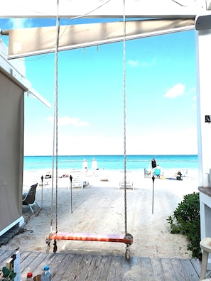 Blick auf einen Strand mit Schaukeln, Liegestühlen und blauem Himmel.