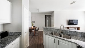 A modern kitchen with granite countertops, a stainless steel sink, and a dining area with a table and chairs. - Landing | Incredible 1BD, Clubhouse, Gym (Murfreesboro)
