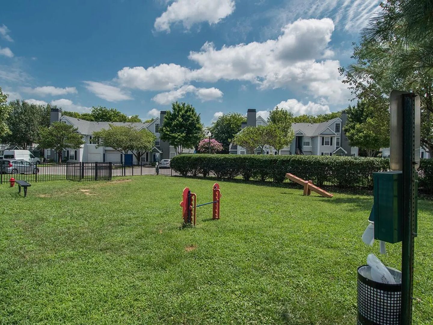 A grassy outdoor area with a playground, a trash can, and a green trash bin.