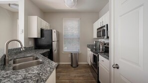 A compact kitchen with a granite countertop, stainless steel appliances, and a window with blinds. - Landing | Beautiful 1BD, Gym, Clubhouse (Murfreesboro)