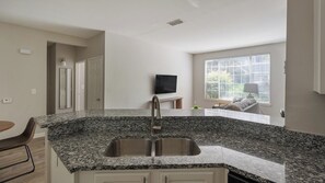 A modern kitchen with granite countertops, stainless steel sink, and a flat-screen TV mounted on the wall. - Landing | Beautiful 1BD, Gym, Clubhouse (Murfreesboro)