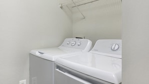 A laundry area with two stacked washers and dryers, a metal drying rack, and a white wall. - Landing | Beautiful 1BD, Clubhouse, Gym (Murfreesboro)