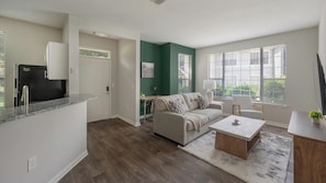 A modern living room with a sofa, coffee table, and a kitchen area with a refrigerator. - Landing | Spectacular 1BD, Clubhouse, Gym (Murfreesboro)