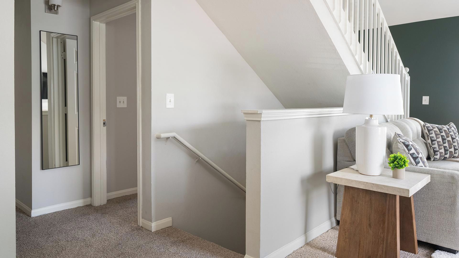 Ein modernes Interieur mit Treppe, Spiegel, Lampe und Sofa.
