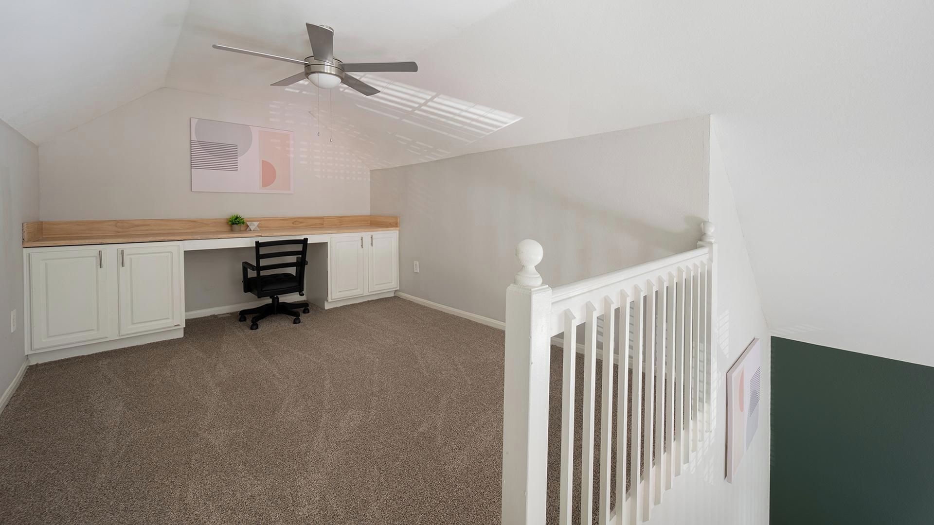 A room with a desk, chair, ceiling fan, and a white railing.