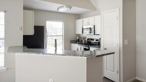 A kitchen with a granite countertop, white cabinets, a black refrigerator, a microwave, and a stove. - Landing | Incredible 1BD, Clubhouse, Gym (Murfreesboro)