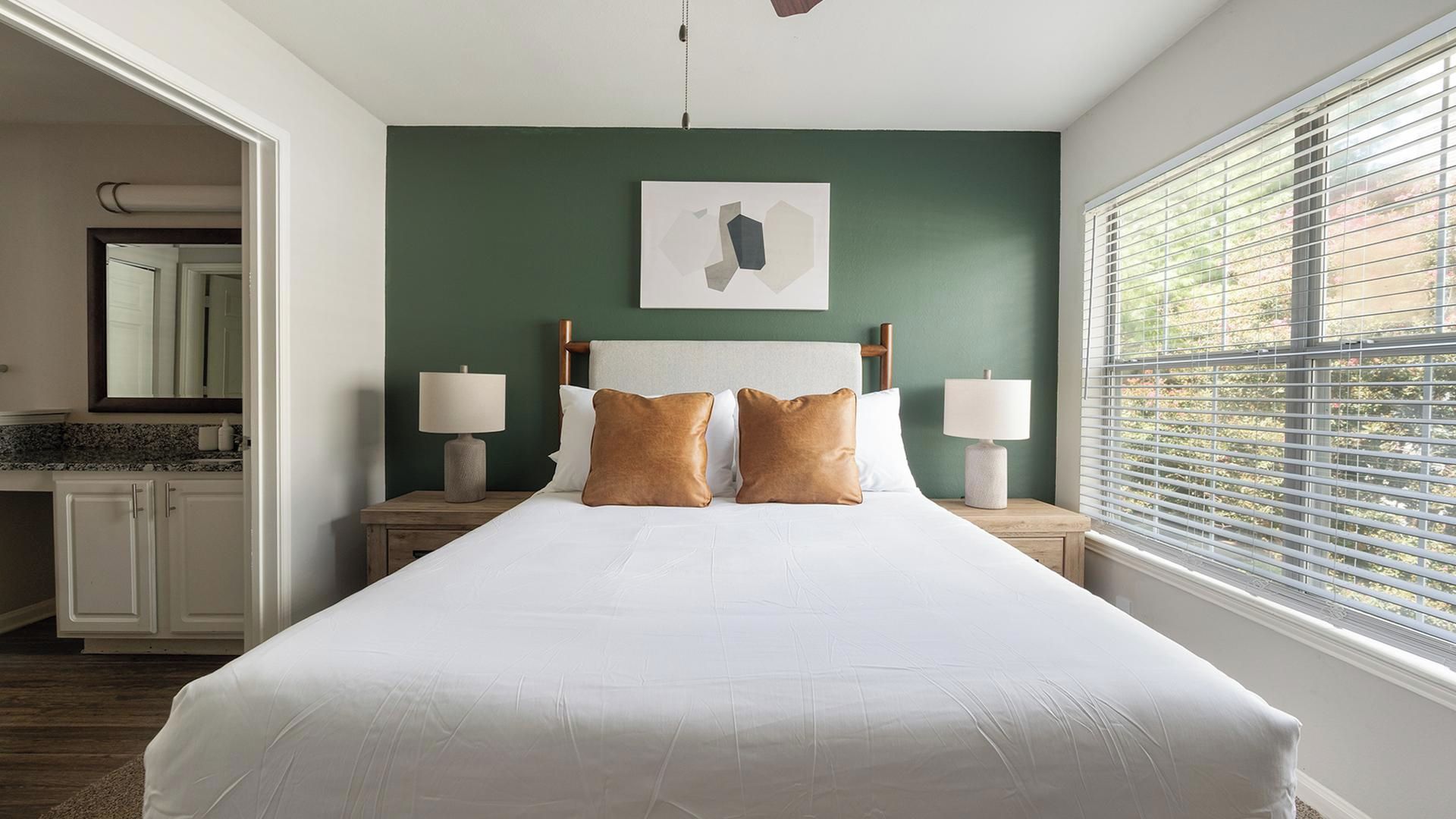 Une chambre à coucher avec un lit, deux lampes de chevet, une table de chevet, un miroir et une fenêtre avec des stores.