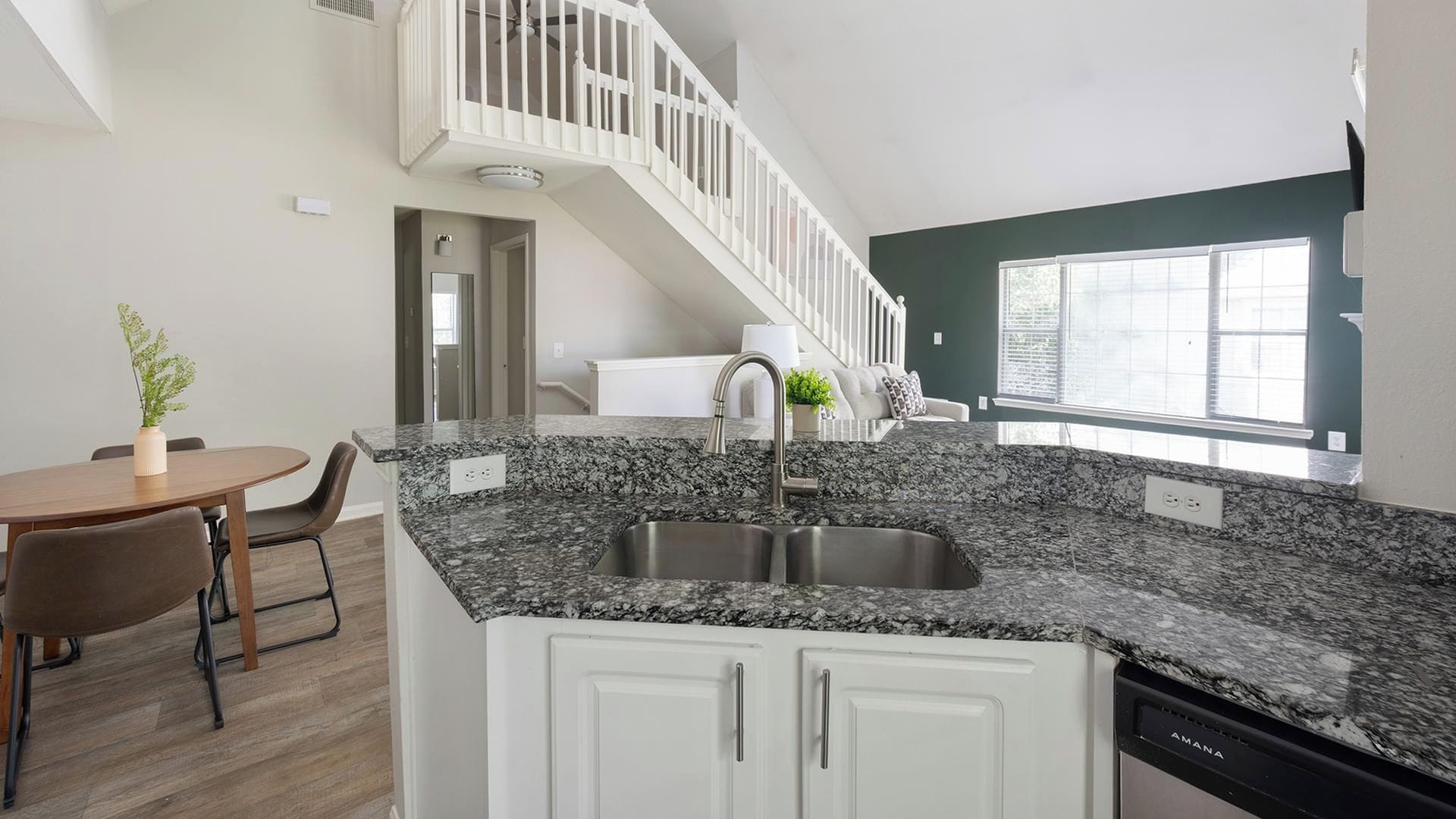 A modern kitchen with granite countertops, a double sink, and white cabinetry.