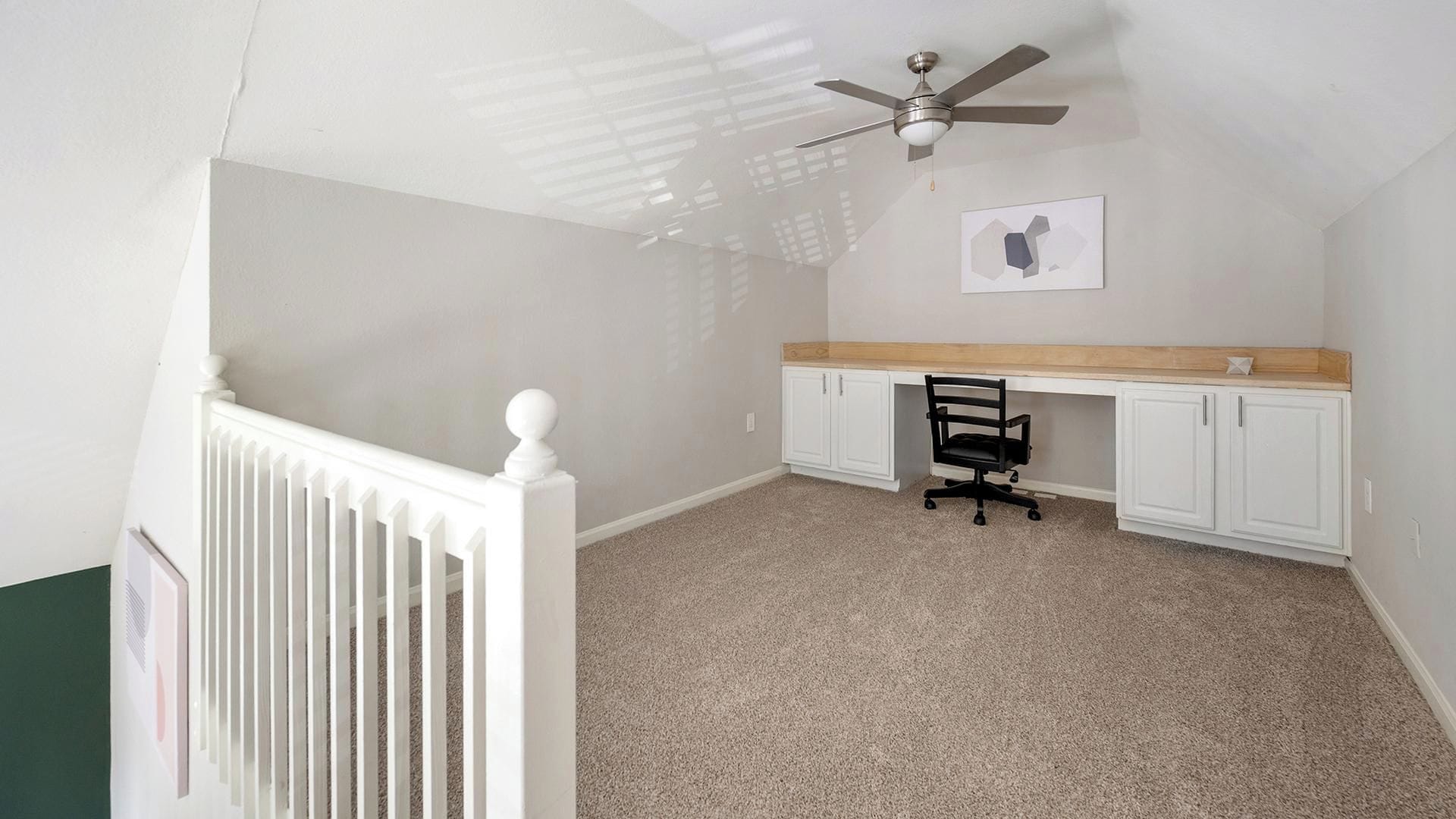 A room with a white radiator, a ceiling fan, a desk with a chair, and a framed picture on the wall.