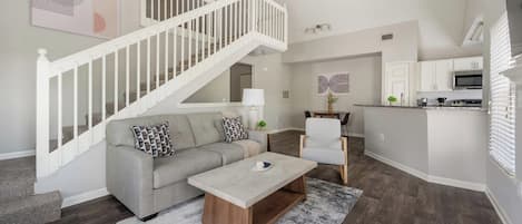 Una sala moderna con escaleras, un sofá, una mesa de centro y una zona de cocina.