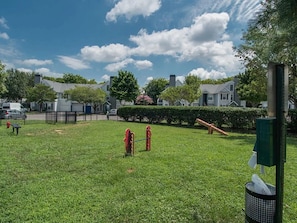 Ein grünes, rasiges Areal mit Spielplatz, Mülleimer und einer grünen Abfalltonne.