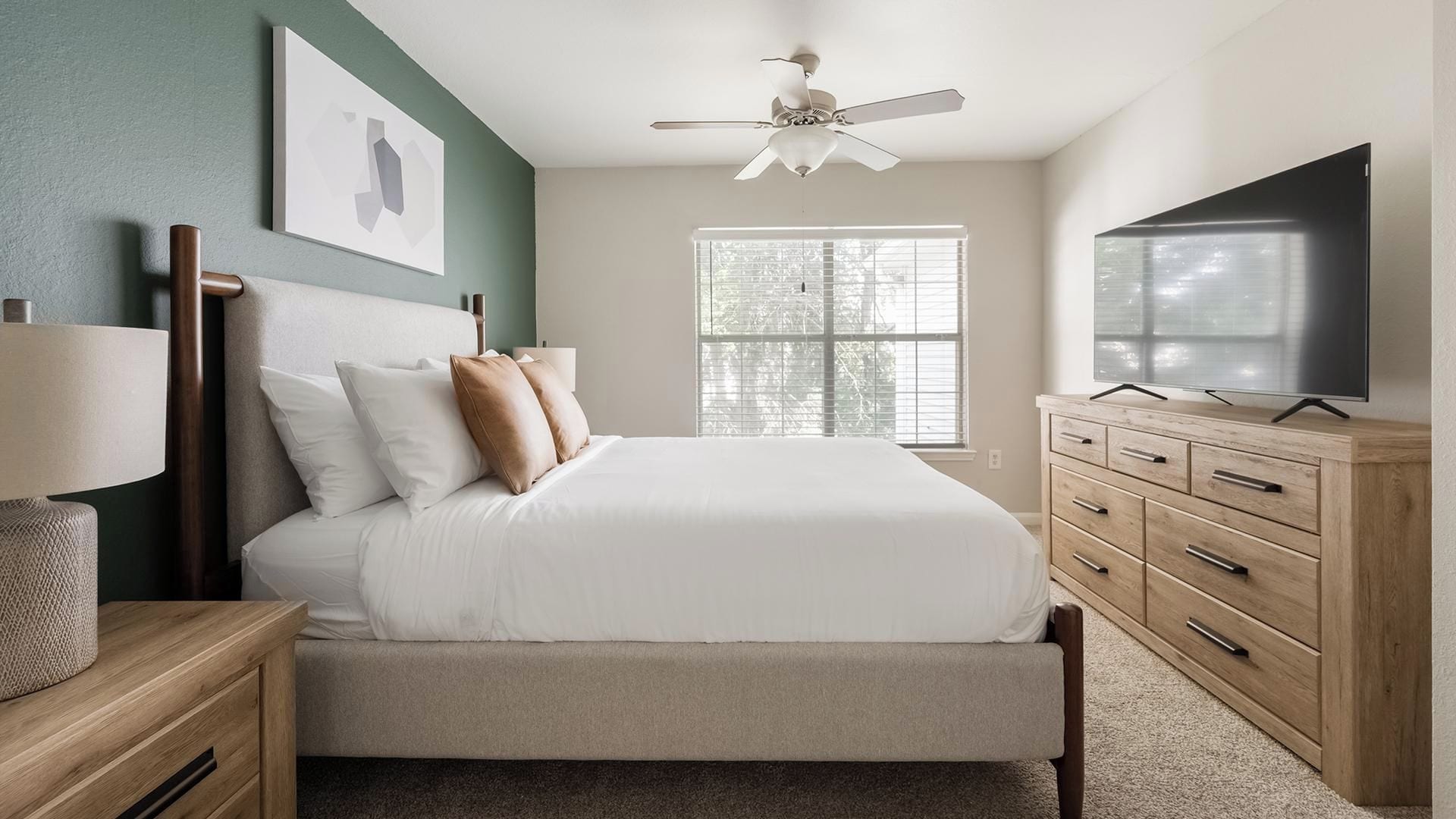 A bedroom with a bed, a ceiling fan, a TV, and a window.