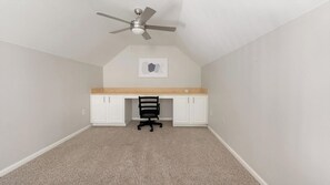 Ein Zimmer mit Deckenventilator, Schreibtisch mit Stuhl und einem gerahmten Bild an der Wand.