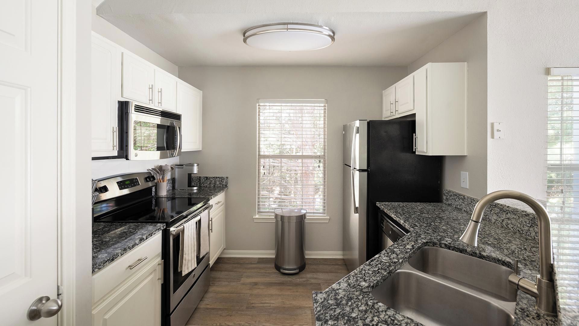 A compact kitchen with white cabinetry, a stainless steel refrigerator, a microwave, and a sink.
