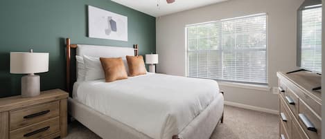A bedroom with a bed, nightstands, a dresser, a ceiling fan, a window with blinds, and a wall-mounted artwork.