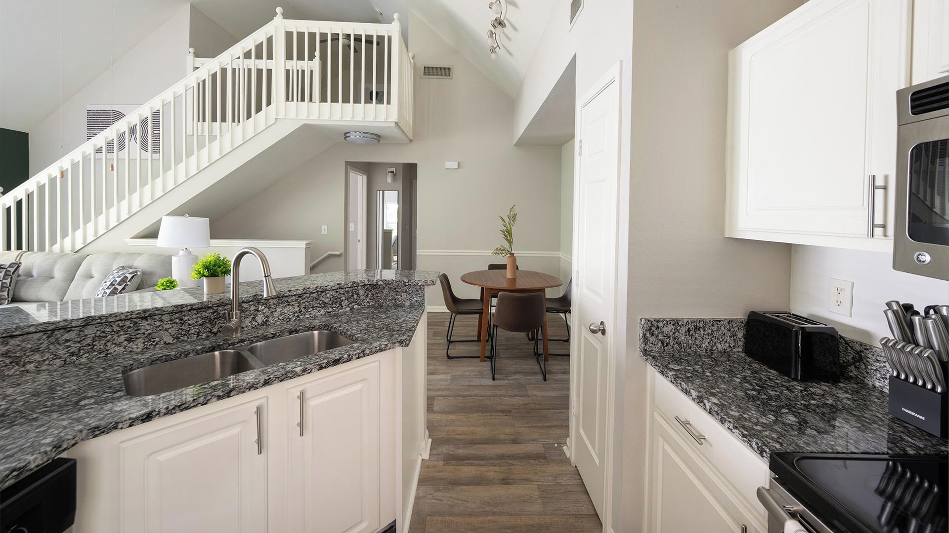 A modern kitchen with granite countertops, stainless steel appliances, and white cabinetry.