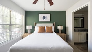 A hotel room with a large bed, two bedside lamps, a ceiling fan, a green accent wall, and a window with blinds. - Landing | Stunning 2BD, Clubhouse, Gym (Murfreesboro)
